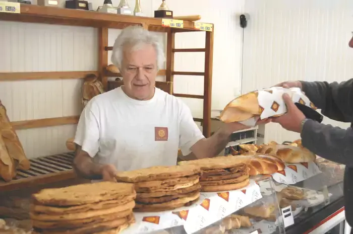 Gérard derrière son éetal de fouaces aux fritons et à l'anis en servant du pain à un client